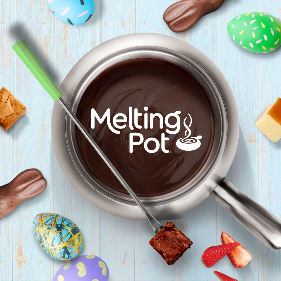 A pot of melted chocolate fondue sits on a light blue wooden surface, with the words “Melting Pot” and a steaming bowl logo appearing on the chocolate. A fondue fork with a green handle dips a brownie piece into the chocolate. Around the pot are Easter-themed treats, including chocolate bunnies, decorated eggs, strawberries, and small cubes of cake.